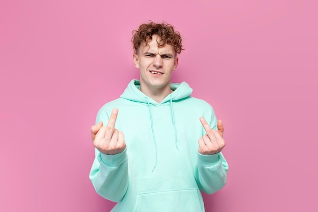 Young rude guy in mint hoodie showing middle finger on pink isolated background