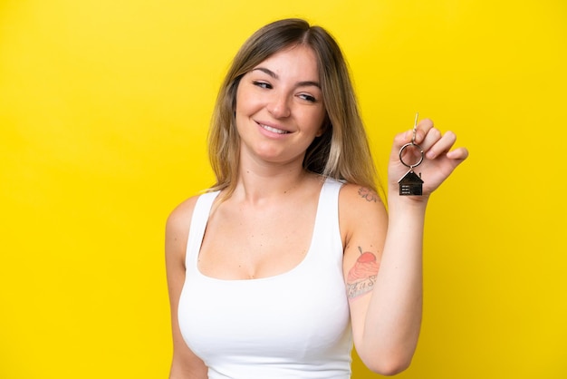 Young rumanian woman holding home keys isolated on yellow background with happy expression