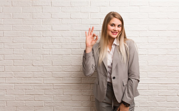 Young russian business woman cheerful and confident doing ok gesture