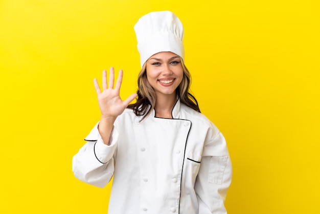 노란색 배경에 격리된 젊은 러시아 요리사 소녀는 손가락으로 다섯을 세고 있습니다.