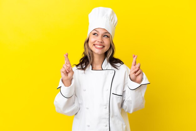 Young Russian chef girl isolated on yellow background with fingers crossing