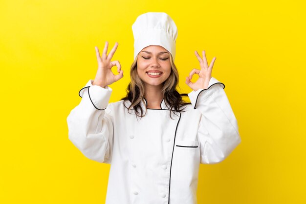 Young russian chef girl isolated on yellow background in zen pose