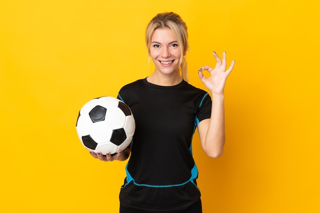 손가락으로 확인 표시를 보여주는 노란색 배경에 고립 된 젊은 러시아 축구 선수 여자