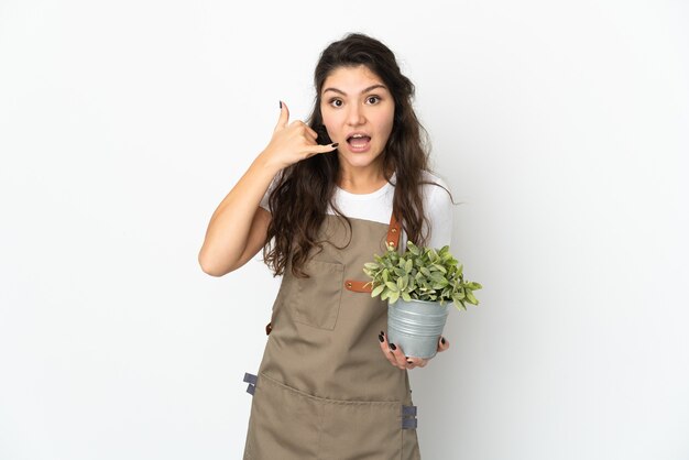 電話ジェスチャーを作る孤立した植物を保持している若いロシアの庭師の女の子