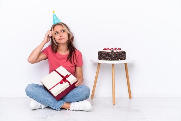 Young Russian girl celebrating a birthday sitting one the floor isolated on white background having doubts and with confuse face expression