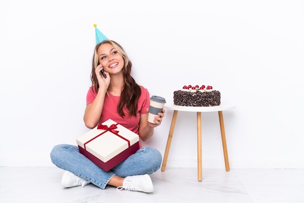 흰색 배경에 격리된 바닥에 앉아 테이크아웃 커피와 모바일을 들고 생일을 축하하는 어린 러시아 소녀