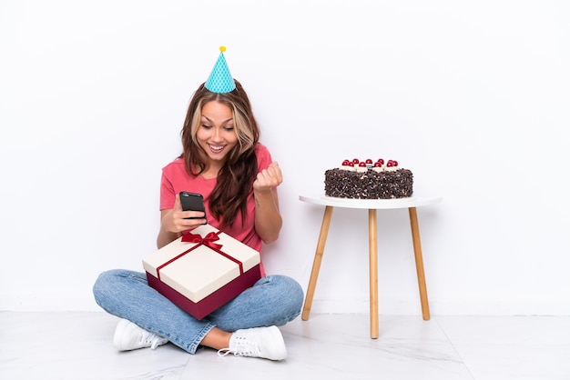 Young Russian girl celebrating a birthday sitting one the floor isolated on white background surprised and sending a message