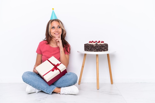 見上げながらアイデアを考えて白い背景で隔離の床に座って誕生日を祝う若いロシアの女の子