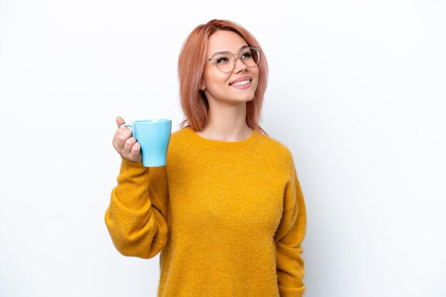 Photo young russian girl holding cup of coffee isolated on white background looking up while smiling