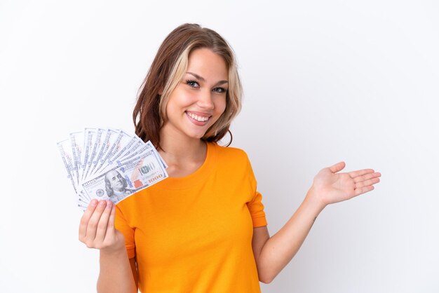 Young Russian girl holding dollars isolated on white background extending hands to the side for inviting to come