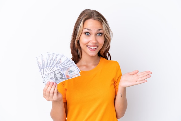 Young Russian girl holding dollars isolated on white background with shocked facial expression