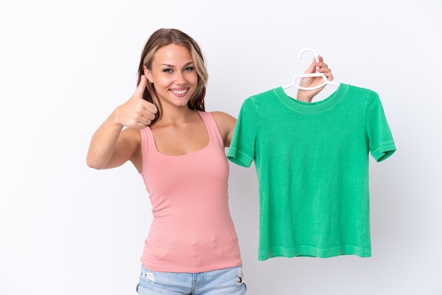 Young Russian girl holding hanger isolated on white background with thumbs up because something good has happened