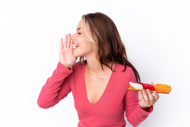 Young Russian girl holding sashimi isolated on white background shouting with mouth wide open to the side