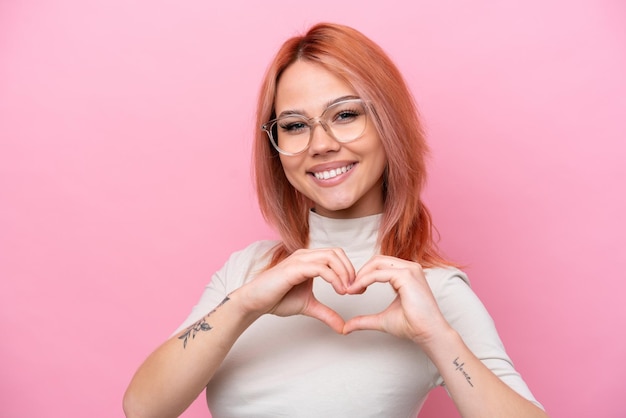 Young Russian girl isolated on pink background With glasses making heart with hands