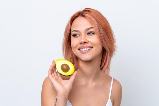 Young Russian girl isolated on white background holding an avocado while smiling Close up portrait