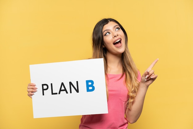 Young Russian girl isolated on yellow background holding a placard with the message PLAN B and thinking