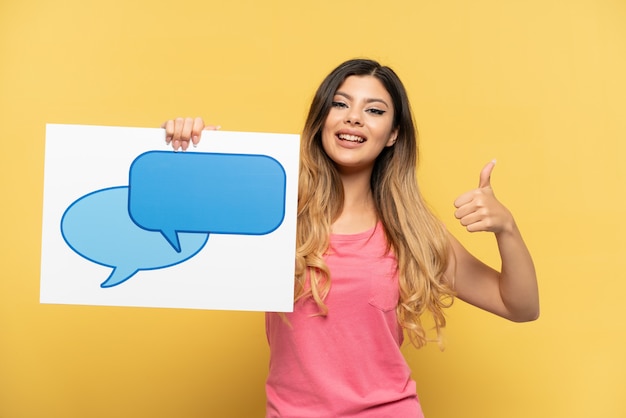 Young Russian girl isolated on yellow background holding a placard with speech bubble icon with thumb up