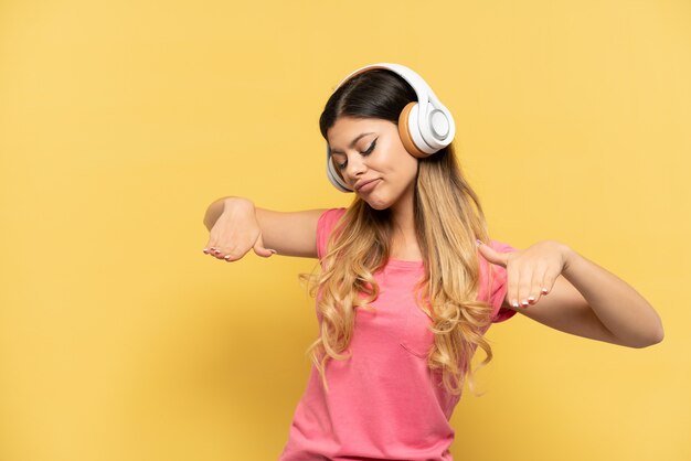 Молодая русская девушка изолирована на желтом фоне, слушает музыку и танцует