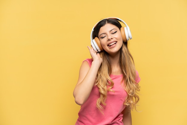 Young Russian girl isolated on yellow background listening music