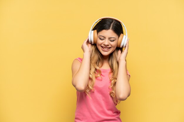 Young Russian girl isolated on yellow wall listening music