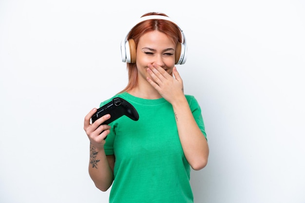 Young Russian girl playing with a video game controller isolated on white background happy and smiling covering mouth with hand