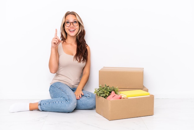 Young Russian girl sitting on the floor isolated on white background pointing up and surprised