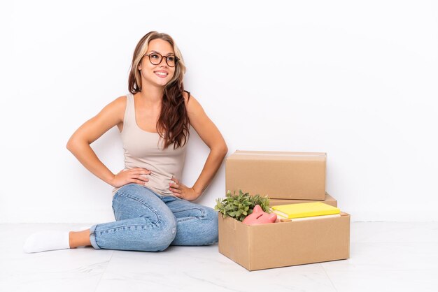 Young Russian girl sitting on the floor isolated on white background posing with arms at hip and smiling