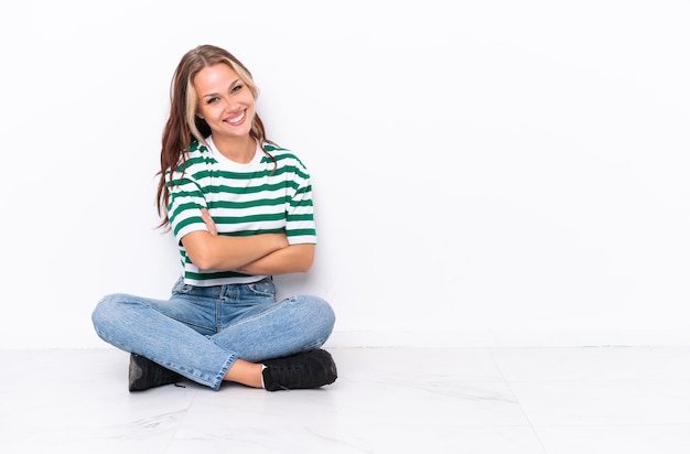 Young Russian girl sitting on the floor isolated on white background with arms crossed and looking forward