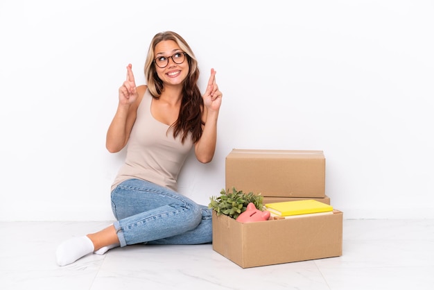 Young Russian girl sitting on the floor isolated on white background with fingers crossing