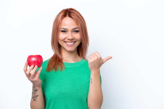 Young Russian girl with an apple isolated on white background pointing to the side to present a product