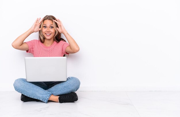 Foto giovane ragazza russa con un computer portatile seduto sul pavimento isolato su sfondo bianco con espressione sorpresa