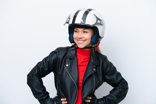 Young Russian girl with a motorcycle helmet isolated on white background posing with arms at hip and smiling