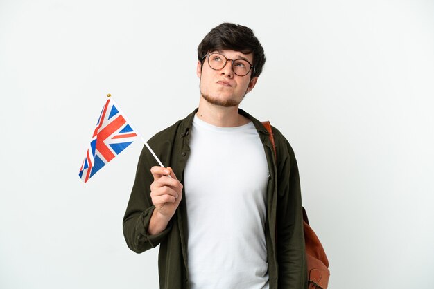 Young Russian man holding an United Kingdom flag isolated on white background and looking up