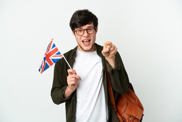 Young Russian man holding an United Kingdom flag isolated on white background surprised and pointing front