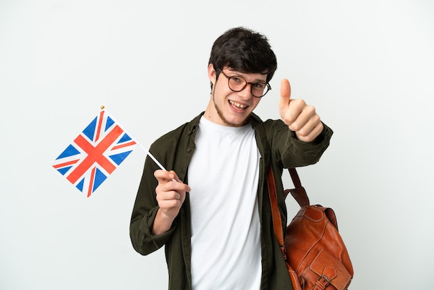 Young Russian man holding an United Kingdom flag isolated on white background with thumbs up because something good has happened