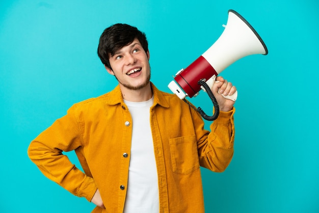 Young Russian man isolated on blue background holding a megaphone and thinking