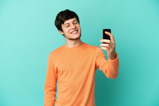 Young Russian man isolated on blue background making a selfie