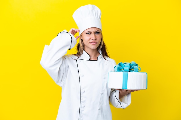 Young Russian pastry chef woman with a big cake isolated on yellow background having doubts