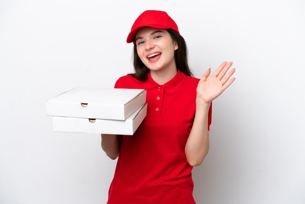 Young Russian pizza delivery picking up pizza boxes isolated on white background saluting with hand with happy expression