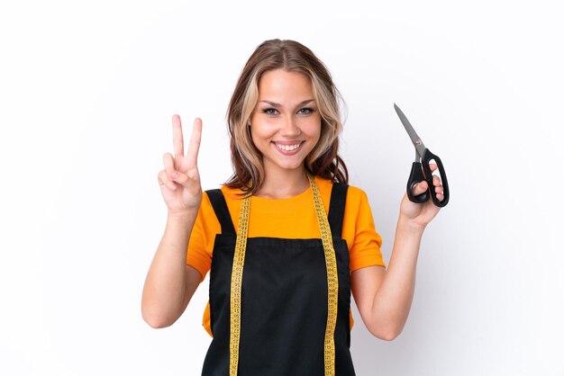 Young Russian seamstress girl isolated on white background smiling and showing victory sign