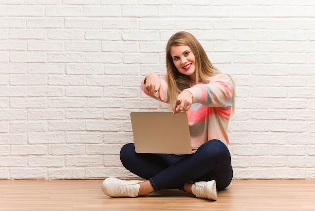 Young russian student woman sitting cheerful and smiling pointing to front