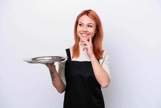 Young Russian waiter with tray isolated on white background thinking an idea while looking up