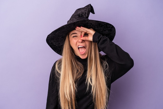 Young Russian woman disguised as a witch celebrating Halloween isolated on purple background excited keeping ok gesture on eye.