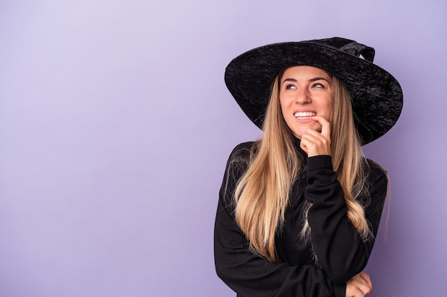 Young Russian woman disguised as a witch celebrating Halloween isolated on purple background relaxed thinking about something looking at a copy space.