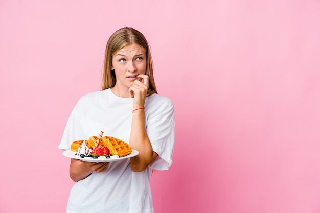 Young russian woman eating a waffle isolated relaxed thinking about something looking at a copy space.