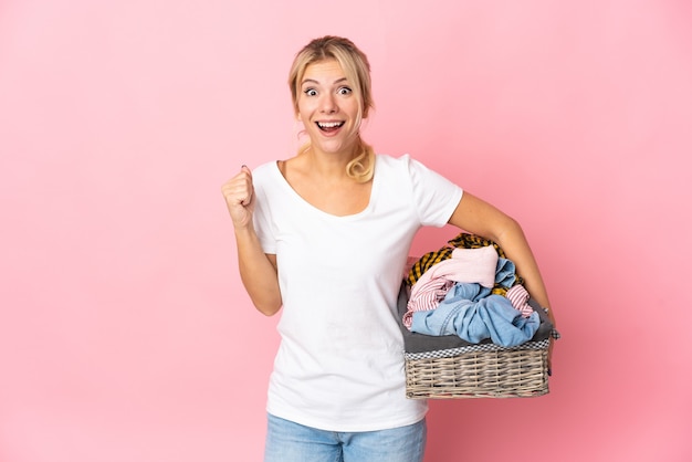 Young Russian woman holding a clothes basket isolated on pink background celebrating a victory in winner position