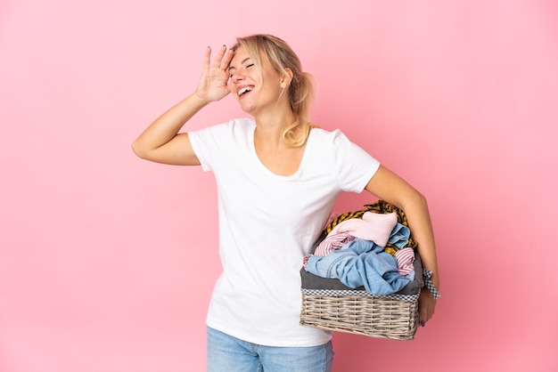 Young Russian woman holding a clothes basket isolated on pink background smiling a lot