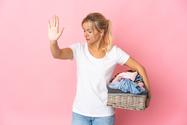 Photo young russian woman holding a clothes basket isolated on pink wall making stop gesture and disappointed