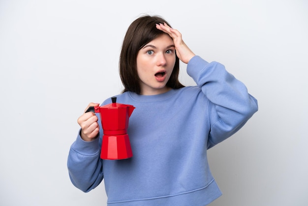 Young Russian woman holding coffee pot isolated on white background doing surprise gesture while looking to the side