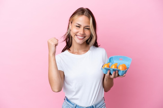 Young Russian woman holding eggs isolated on pink background celebrating a victory